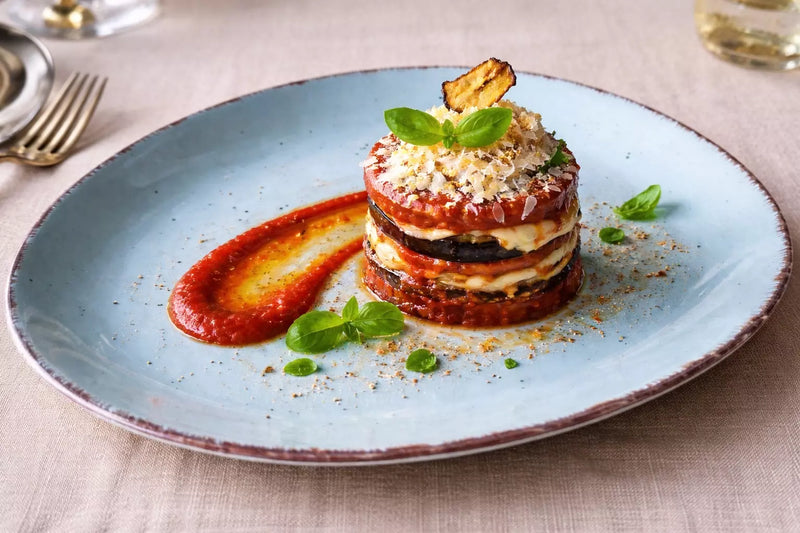 Melanzane alla Parmigiana mit Auberginen, Tomatensauce und Käse auf einem Teller angerichtet