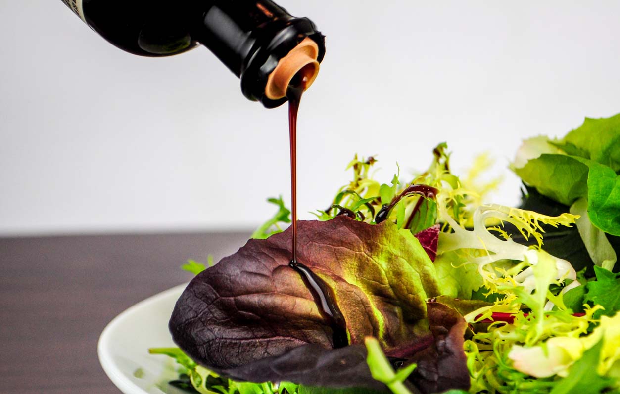 Balsamico Essig wird über frischen gemischten Salat gegossen