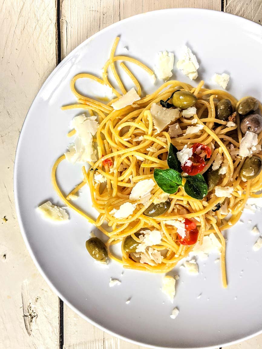 Spaghetti Aglio e Olio mit Oliven, Chili, frischem Basilikum und geriebenem Käse auf weißem Teller