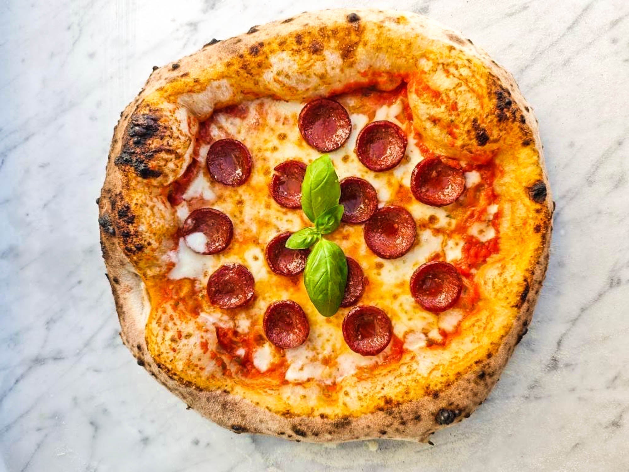 Neapolitanische Pizza mit Salami, Mozzarella und frischem Basilikum auf Marmorplatte