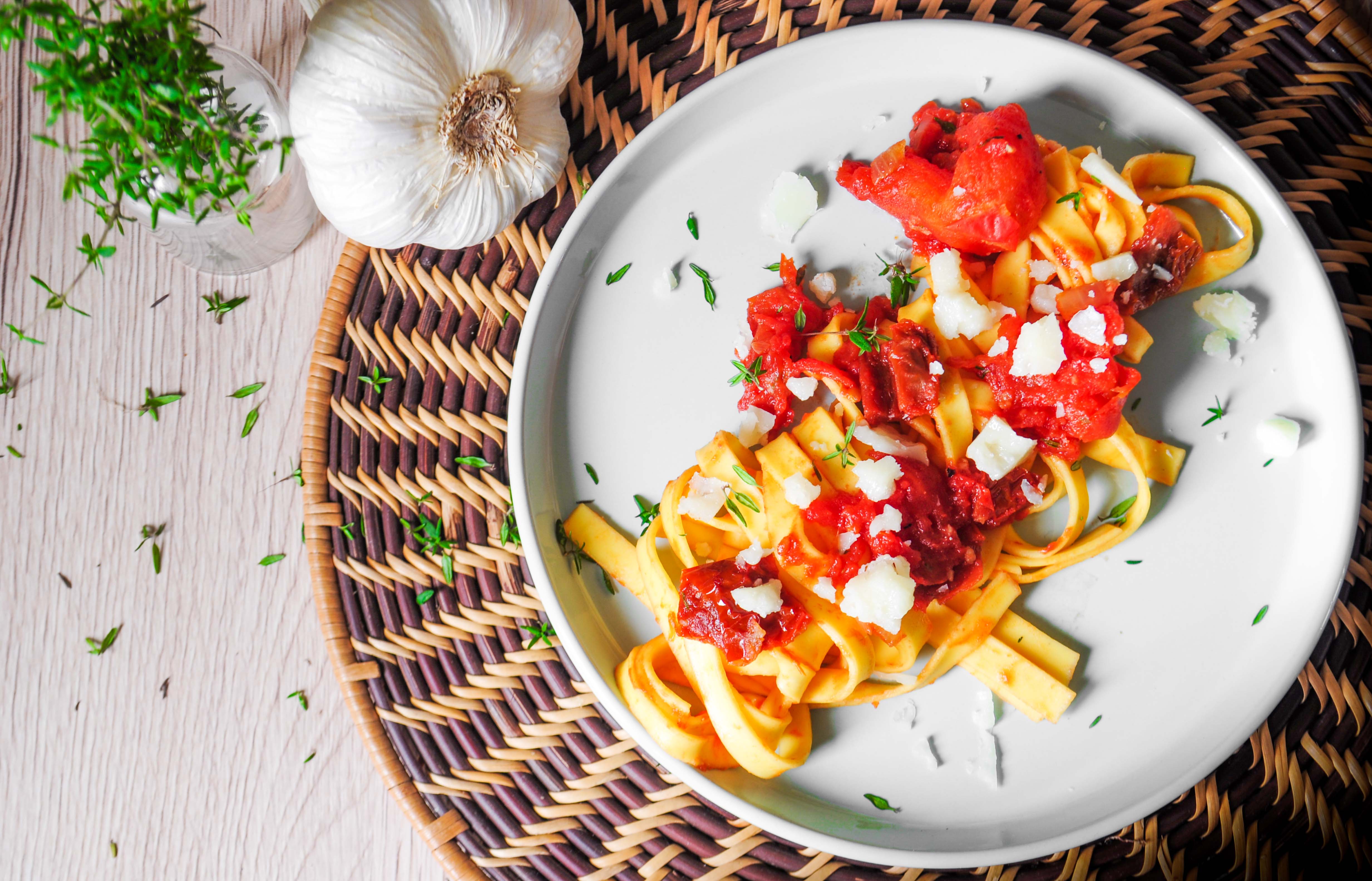 Italienische Tagliatelle mit Tomatensauce, frischem Käse und Kräutern auf weißem Teller