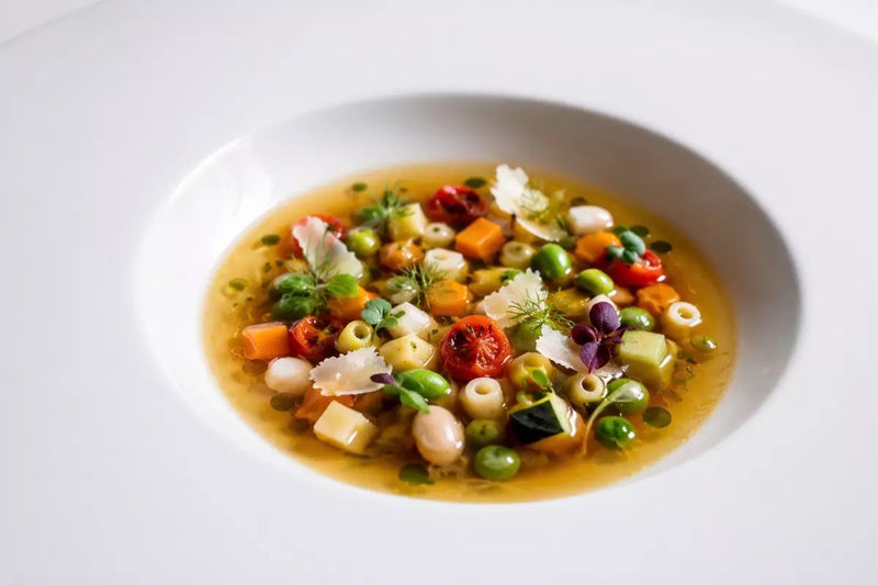 Minestrone mit Gemüsewürfeln, weißen Bohnen, Ditalini-Pasta, Parmigiano Reggiano und Basilikumöl