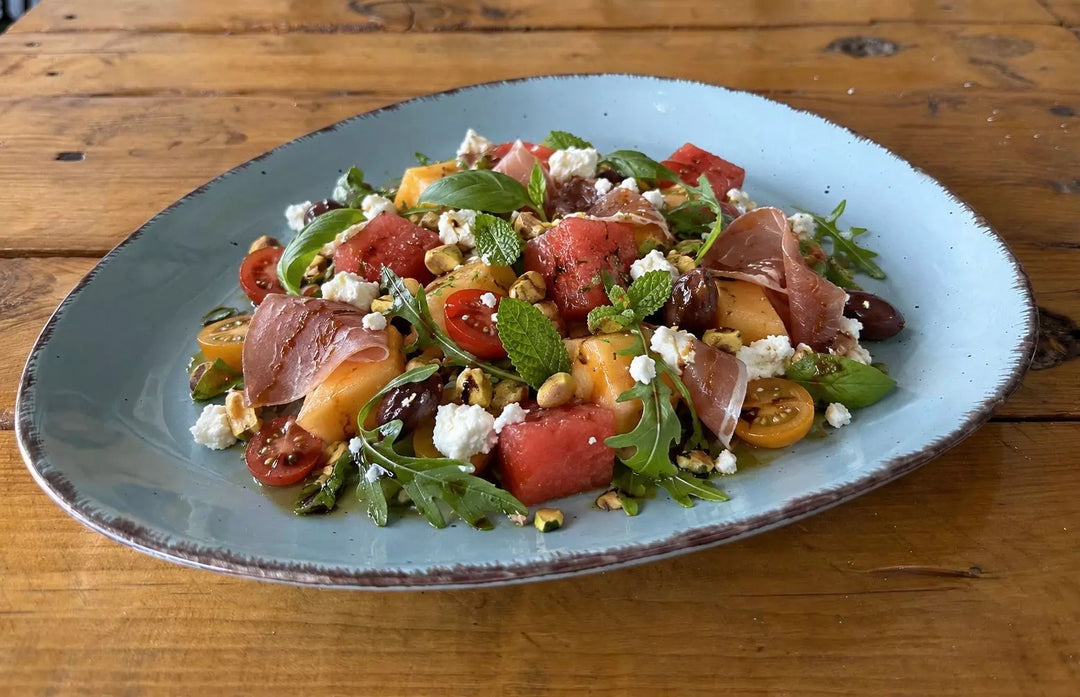 Mediterraner Sommersalat mit Melone, Kirschtomaten, Schafskäse, Prosciutto, Oliven und frischen Kräutern