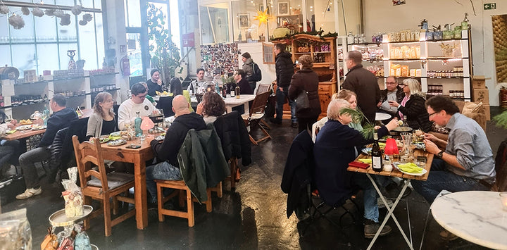 Gemütliches italienisches Feinkostgeschäft mit Gästen beim Essen und Regalen voller Spezialitäten.