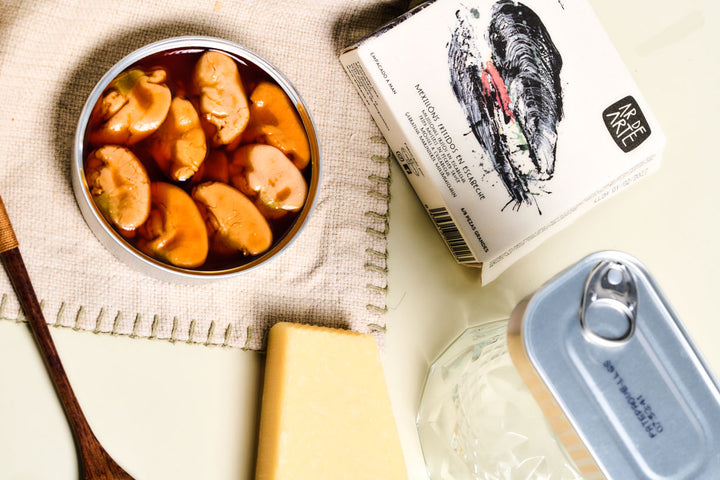 Offene Dose Miesmuscheln in Marinade, daneben Käse und Verpackung, spanische Delikatesse
