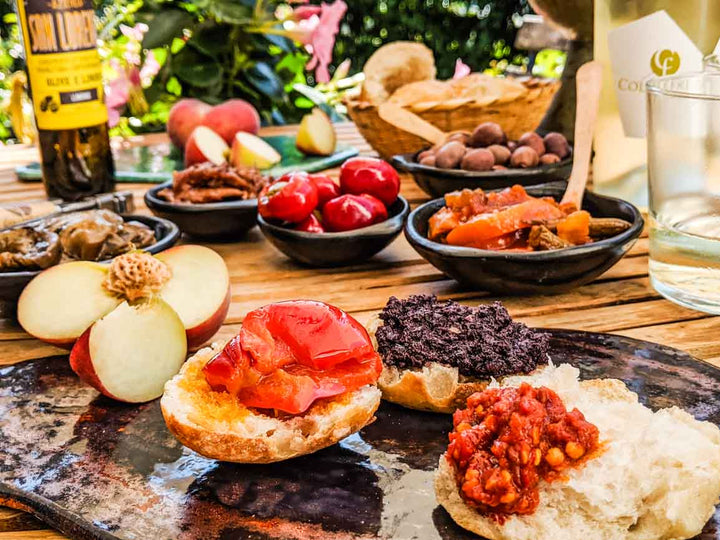 Italienische Antipasti mit Brot, Oliven, eingelegtem Gemüse, Paprika und frischem Obst im Garten