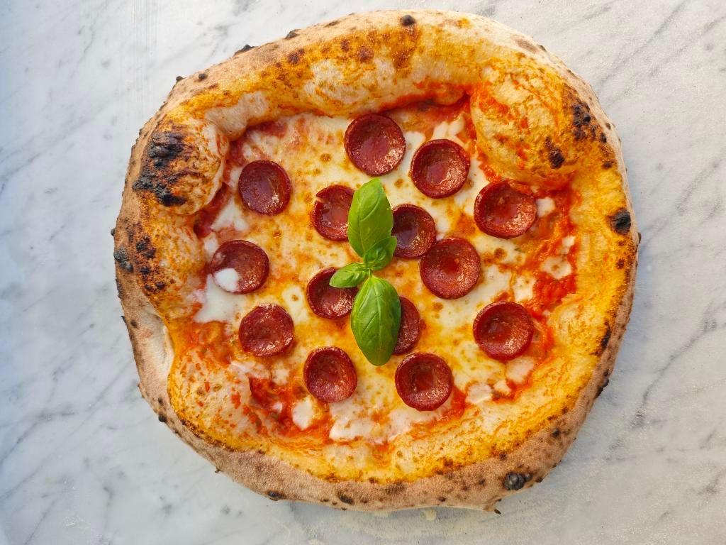 Italienische Pizza mit knusprigem Rand, Salami, Mozzarella, Tomatensauce und Basilikum
