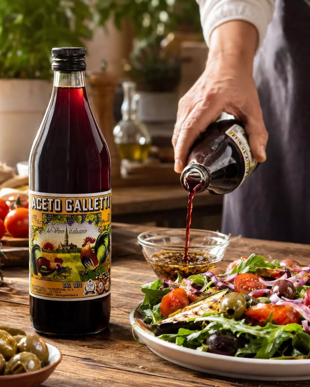 Aceto Galletti Rotweinessig beim Anrühren eines mediterranen Salatdressings mit Gemüse und Oliven