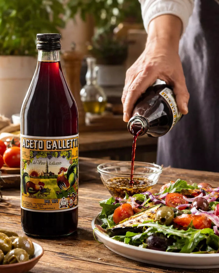 Aceto Galletti Rotweinessig beim Anrühren eines mediterranen Salatdressings mit Gemüse und Oliven
