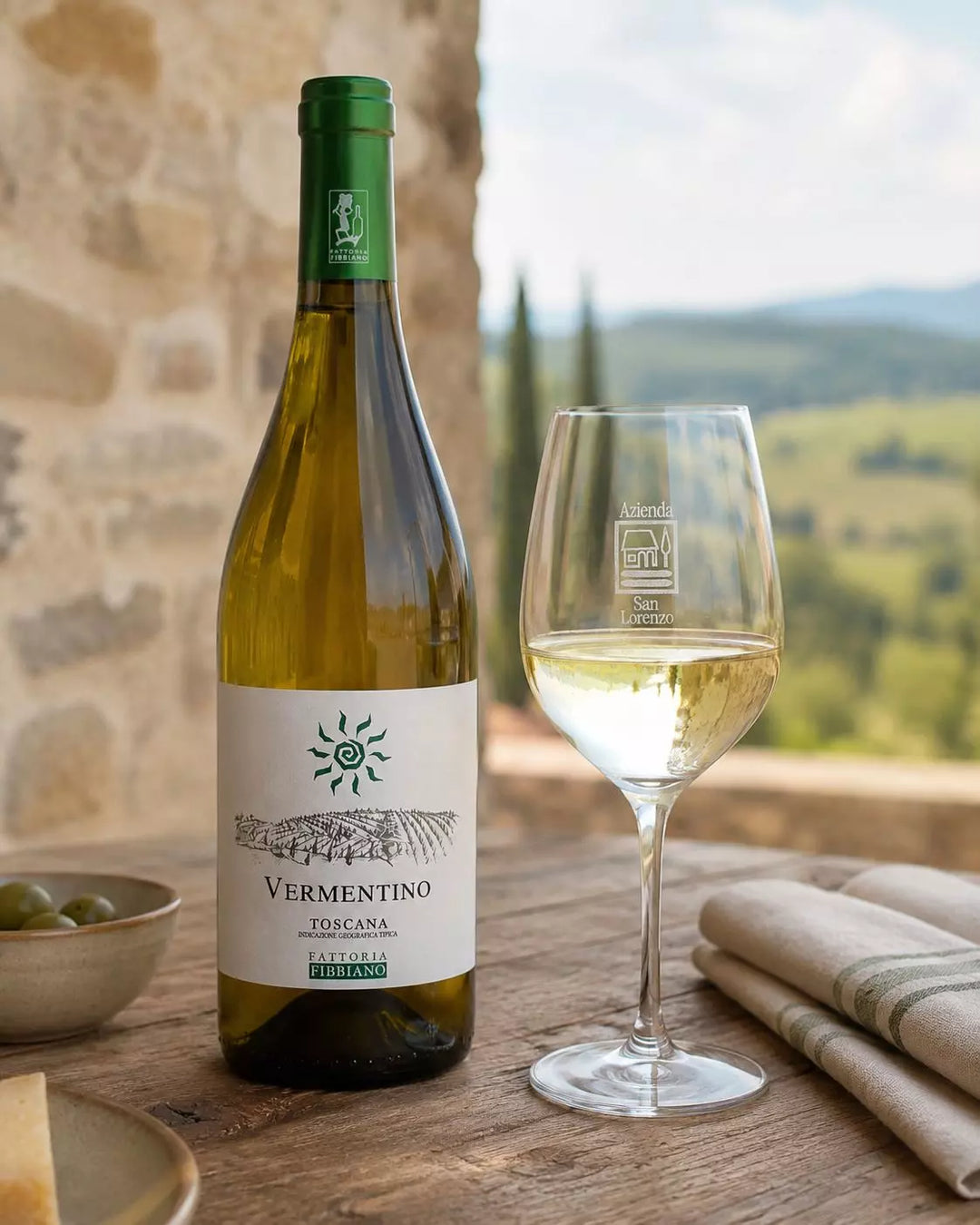 Gefülltes Weinglas der Azienda San Lorenzo neben einer Flasche Fattoria Fibbiano Vermentino in einer toskanischen Tischszene.