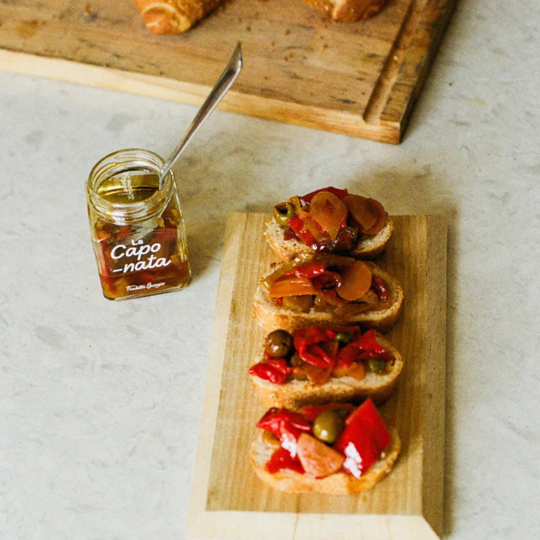 Caponata Gemüse-Antipasti auf Brot, daneben Glas mit gemischtem Gemüse in Öl