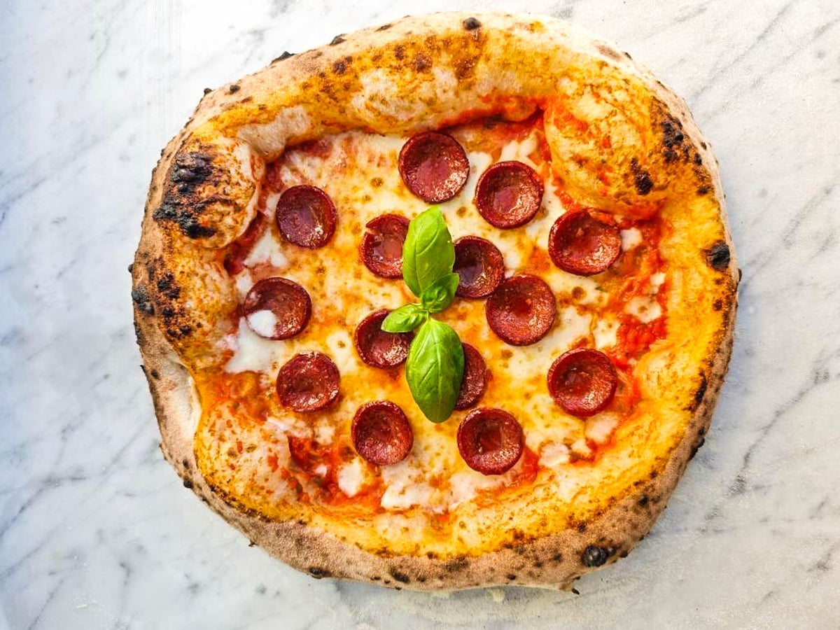 Neapolitanische Pizza mit Salami, Mozzarella und frischem Basilikum auf Marmorplatte