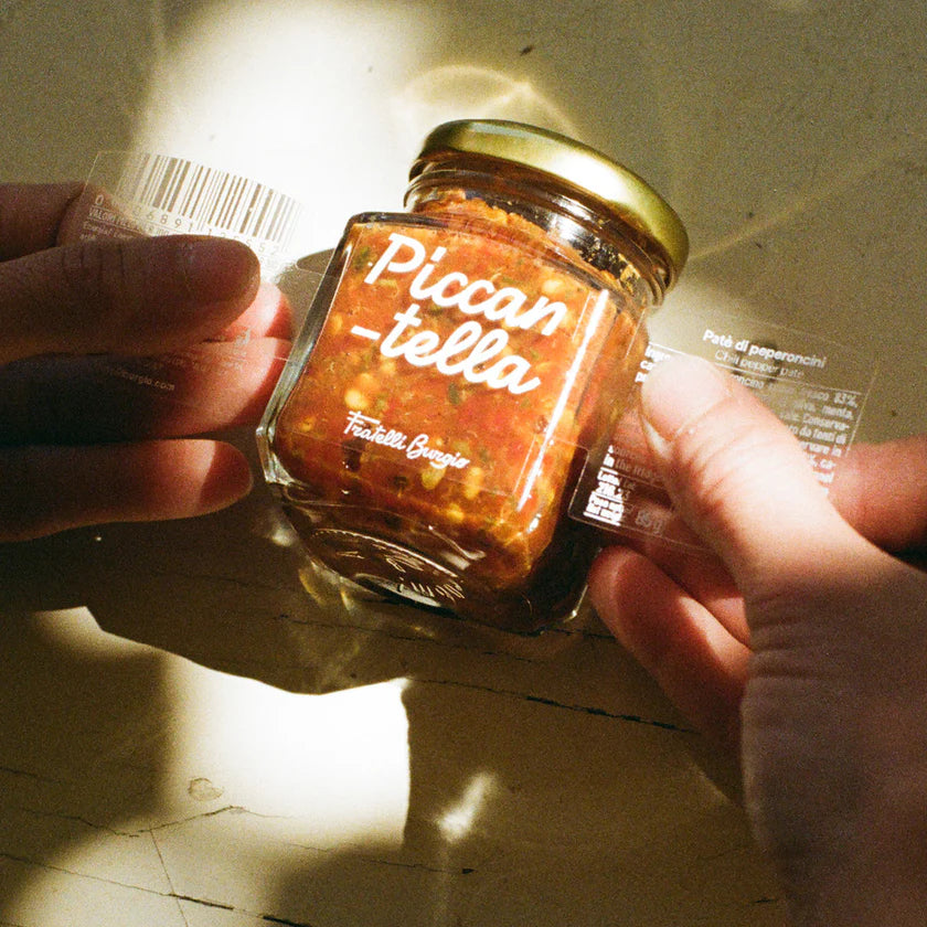 Sizilianische Chili-Paste im Glas mit goldfarbenem Deckel, von zwei Händen gehalten