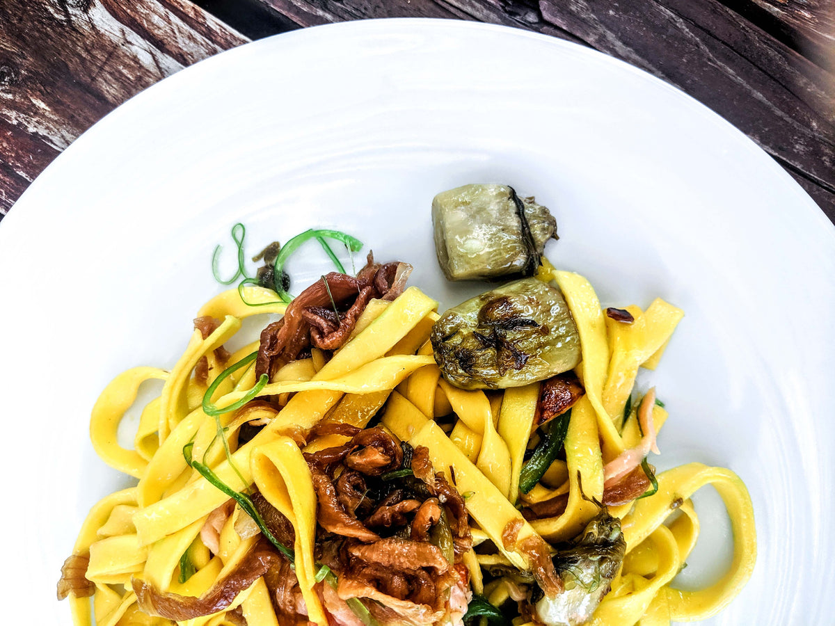 Frische Tagliatelle mit Puntarelle, Zwiebeln und Artischocken auf weißem Teller, italienische Spezialität