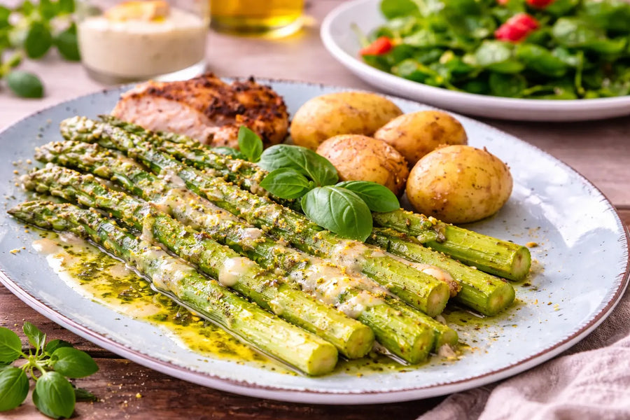 Grüner Spargel mit Crème-Fraîche-Beurre-Blanc, Spargelöl und frischen Kräutern auf Teller angerichtet