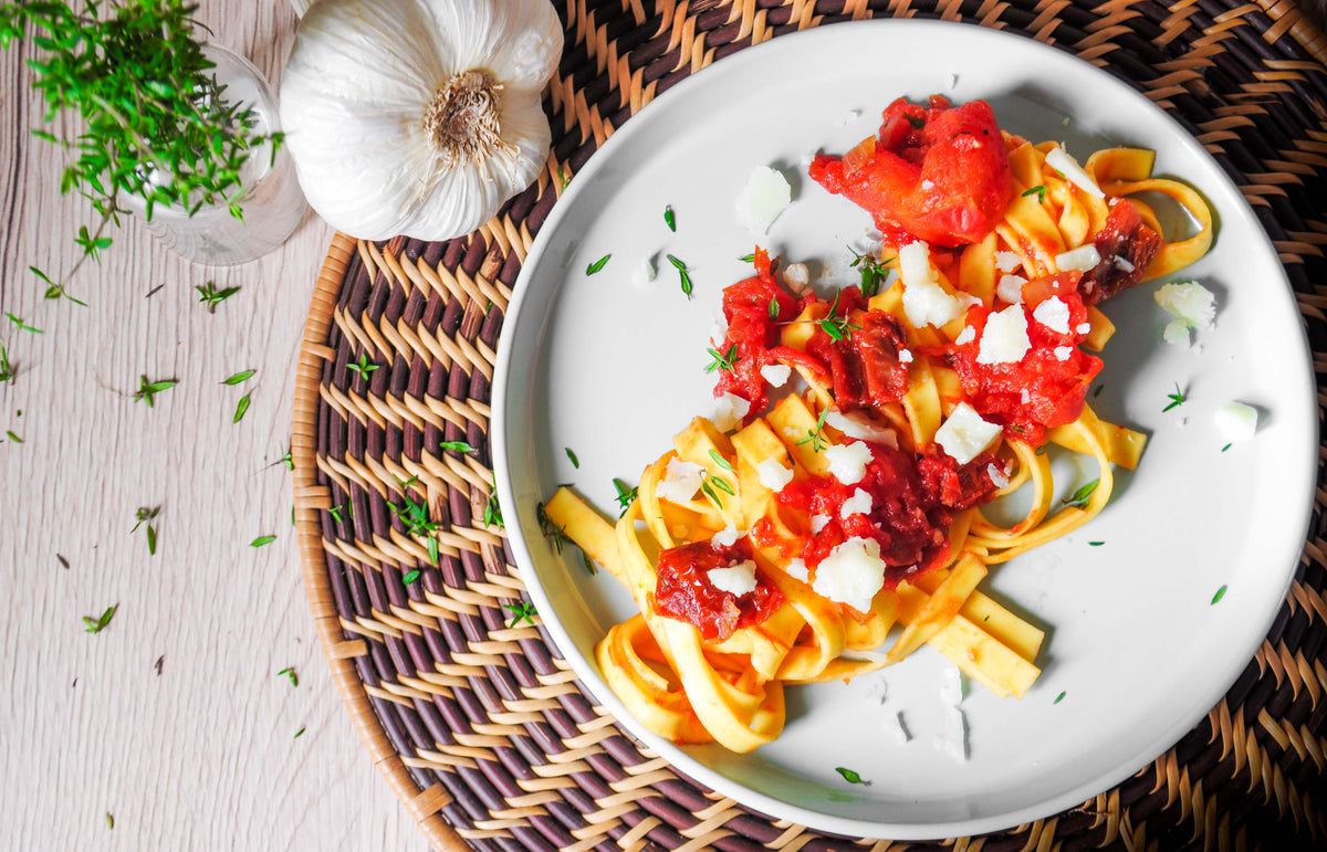 Italienische Tagliatelle mit Tomatensauce, frischem Käse und Kräutern auf weißem Teller